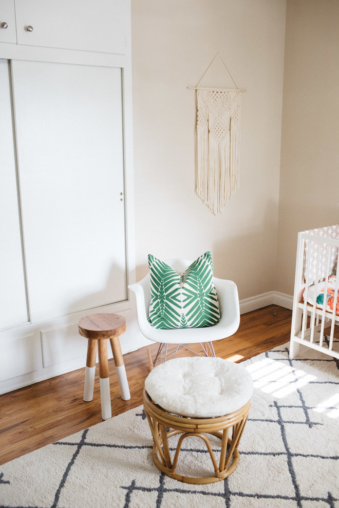 Modelo de habitación de bebé neutra ecléctica de tamaño medio con paredes beige y suelo de madera en tonos medios