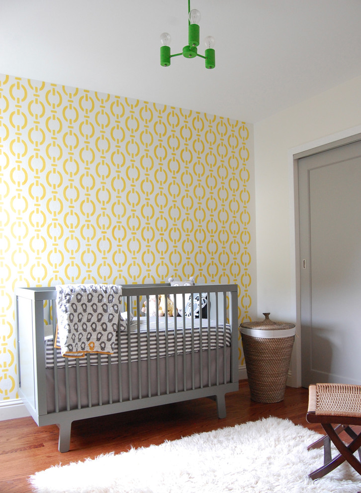 Inspiration pour une petite chambre de bébé neutre design avec un mur jaune et un sol en bois brun.