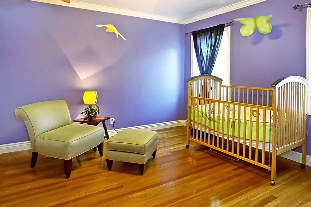 Modelo de habitación de bebé niña actual con paredes púrpuras y suelo de madera en tonos medios