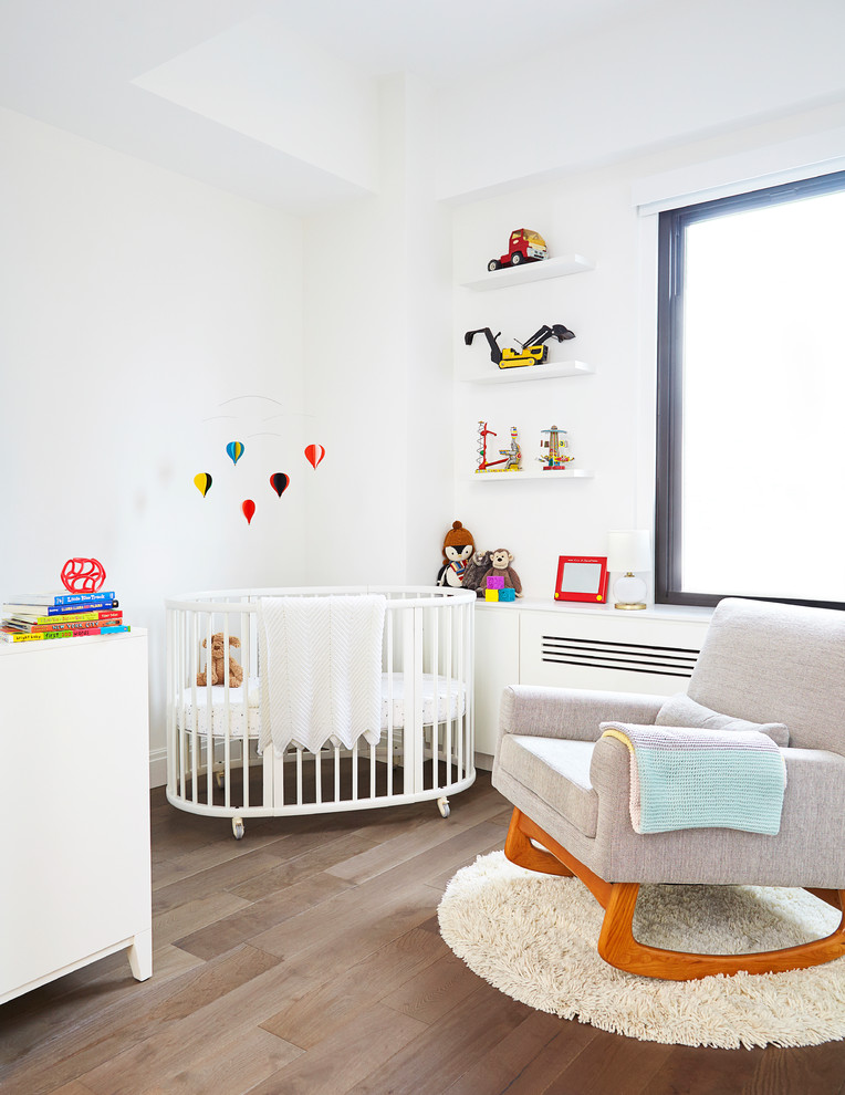 Imagen de habitación de bebé neutra actual pequeña con paredes blancas y suelo de madera en tonos medios