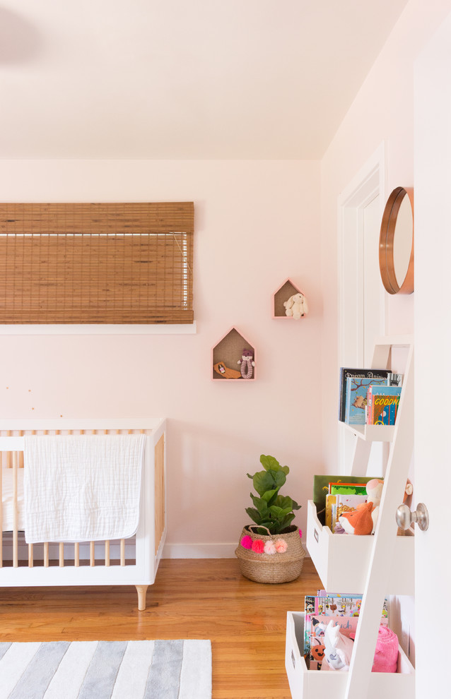 Imagen de habitación de bebé niña ecléctica pequeña con paredes rosas, suelo de madera clara y suelo amarillo