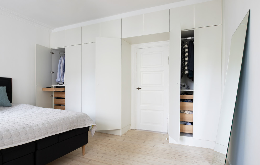 На фото: шкаф в нише унисекс в скандинавском стиле с плоскими фасадами, белыми фасадами и светлым паркетным полом