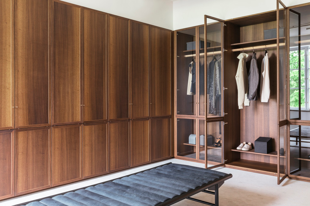 This is an example of a large contemporary gender neutral walk-in wardrobe in Copenhagen with shaker cabinets, medium wood cabinets, carpet and beige floors.