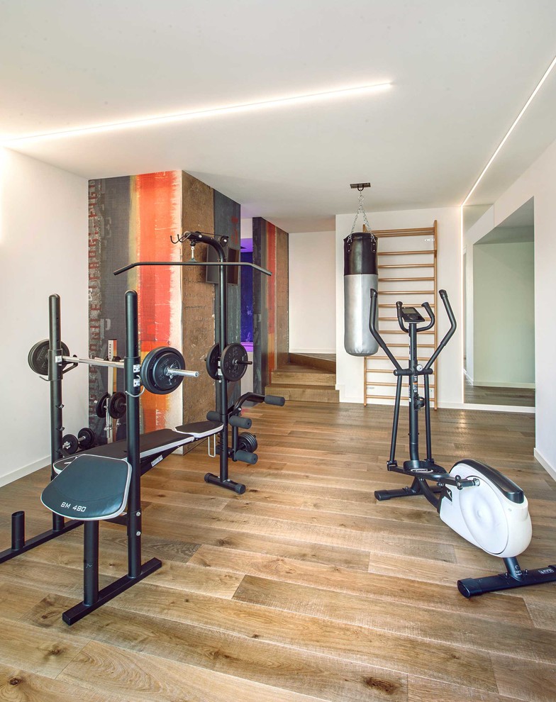 Modern home weight room in Other with white walls and light hardwood flooring.