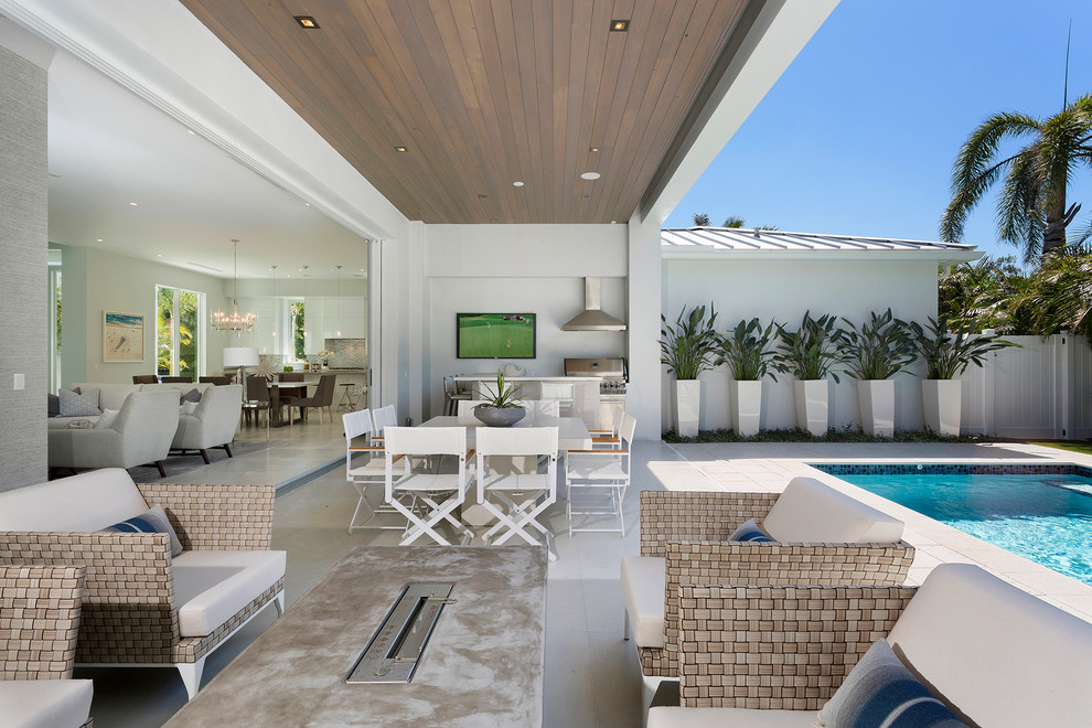Cette image montre une terrasse arrière design de taille moyenne avec une cuisine d'été, une extension de toiture et des pavés en béton.