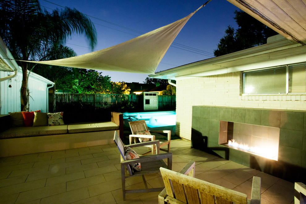 Idée de décoration pour une terrasse arrière vintage de taille moyenne avec un foyer extérieur, du carrelage et un auvent.