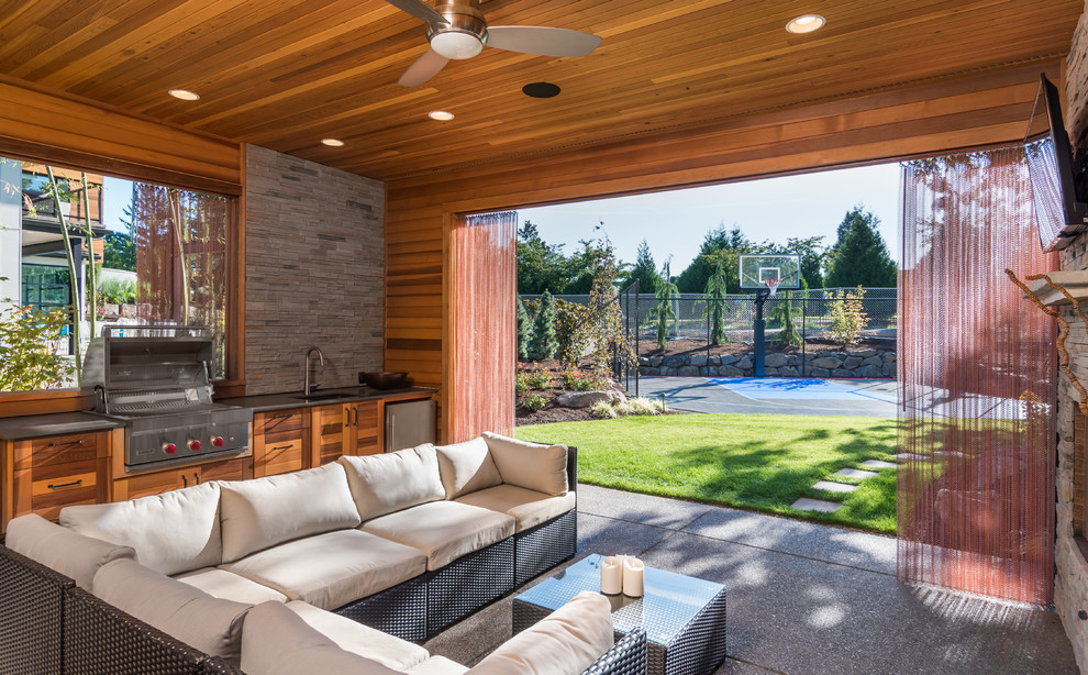 Cette image montre une grande terrasse arrière design avec une cuisine d'été, une dalle de béton et une extension de toiture.
