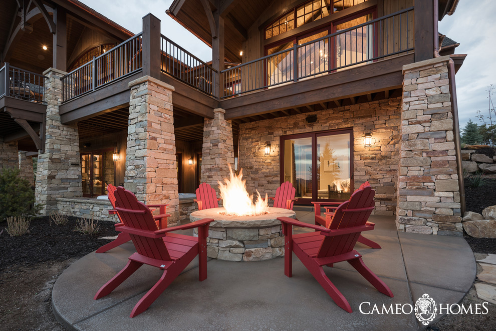 This is an example of a large rustic back patio in Salt Lake City with a fire feature, concrete paving and a roof extension.