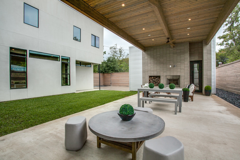 Foto di un grande patio o portico minimalista dietro casa con un focolare, lastre di cemento e un tetto a sbalzo