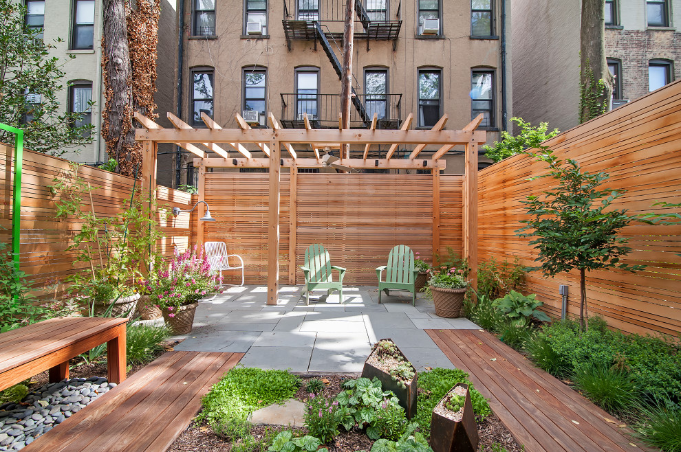 This is an example of a small contemporary back patio in New York with natural stone paving and a pergola.