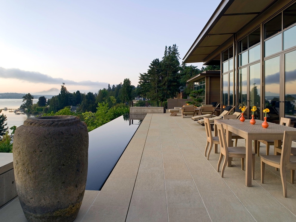 Réalisation d'une terrasse design avec du carrelage et une extension de toiture.