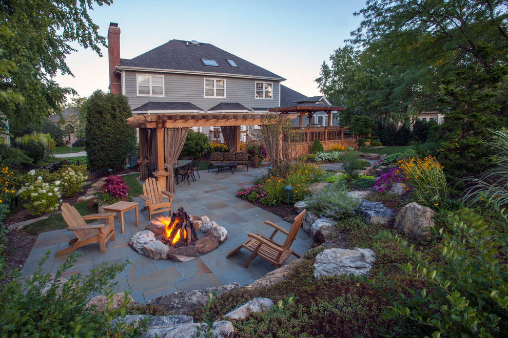 Example of a classic backyard stone patio design in Chicago with a fire pit and a pergola