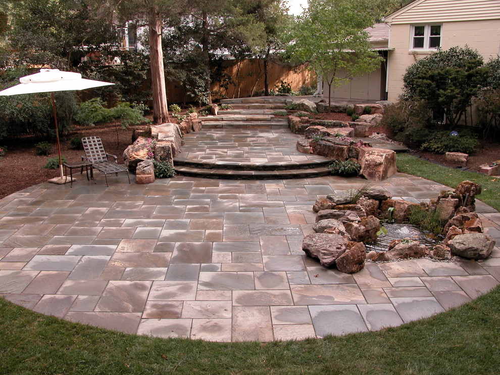 Diseño de patio actual grande en patio trasero con fuente y adoquines de piedra natural