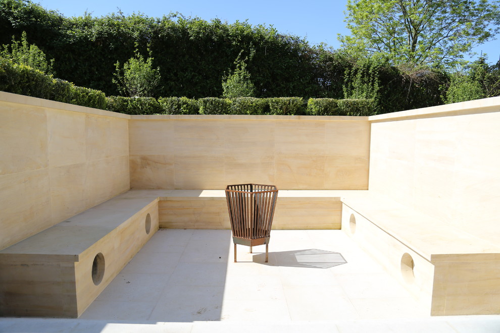This is an example of a medium sized contemporary back patio in Gloucestershire with a fire feature and no cover.