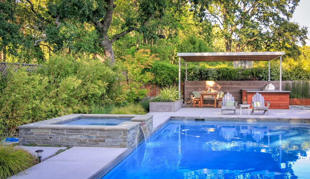 Cette image montre une grande terrasse arrière design avec une cuisine d'été et des pavés en béton.