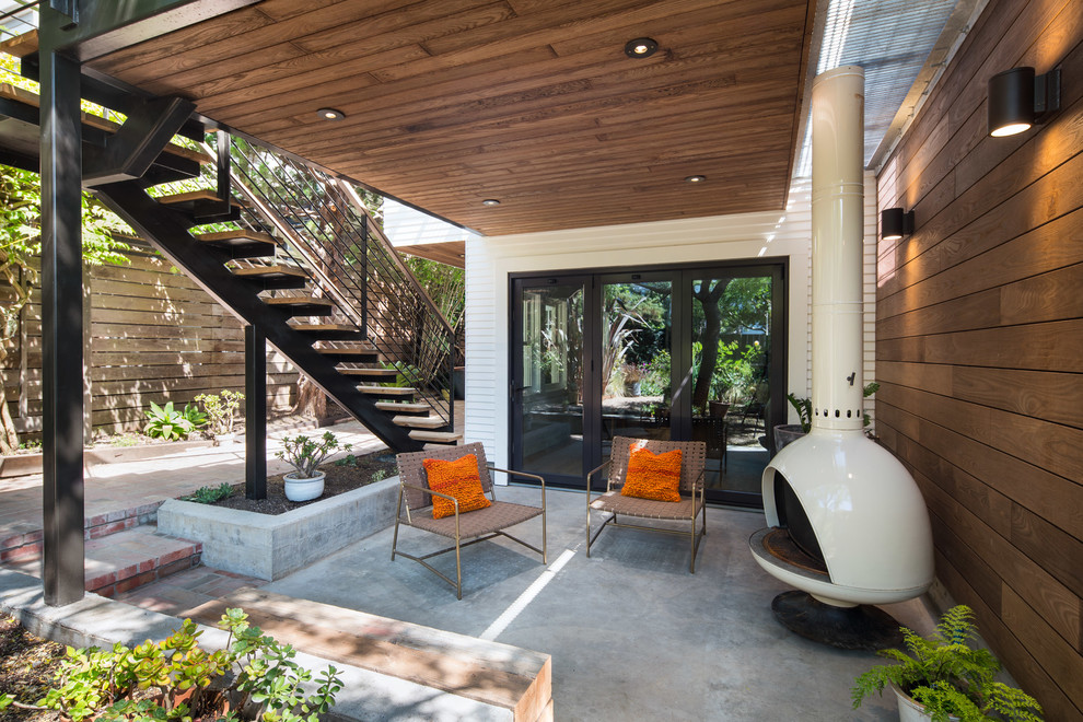 На фото: двор на заднем дворе в современном стиле с покрытием из бетонных плит, навесом и уличным камином с