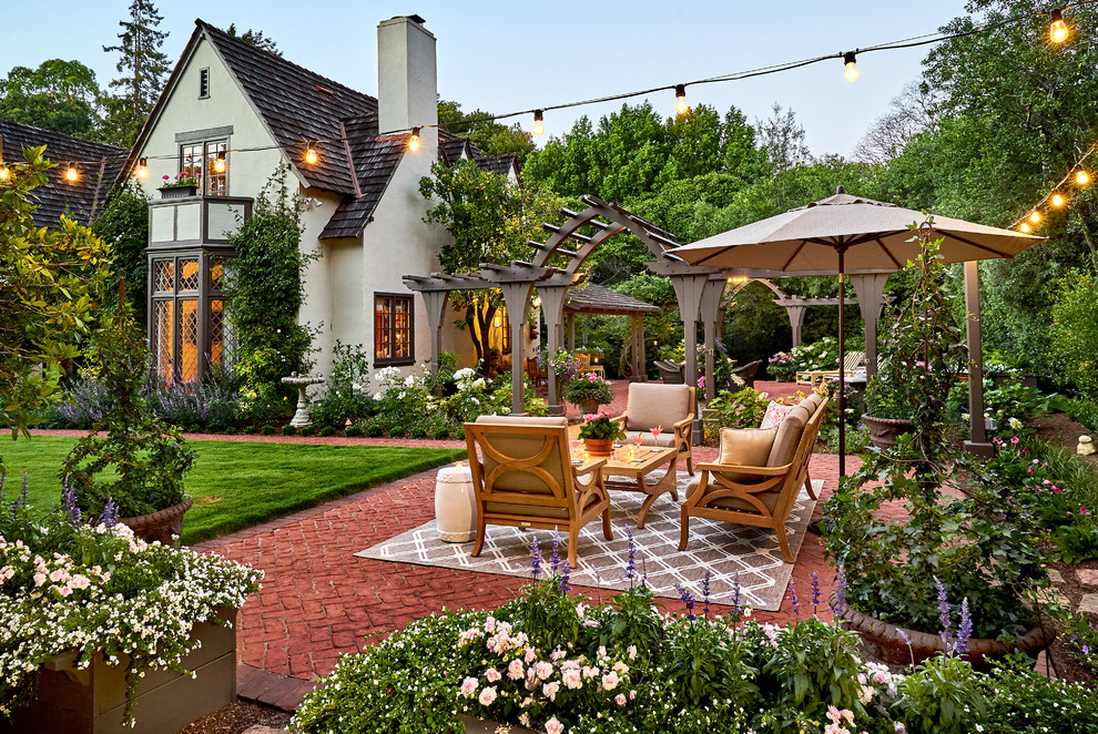 Foto di un ampio patio o portico chic dietro casa con un focolare, pavimentazioni in mattoni e una pergola