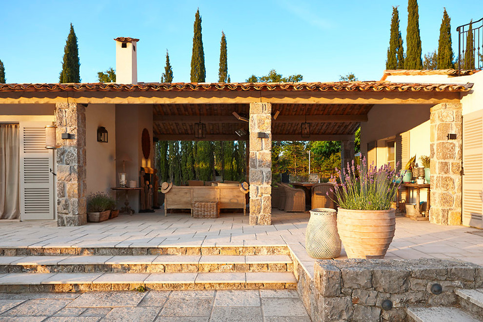 Ispirazione per un patio o portico mediterraneo di medie dimensioni e nel cortile laterale con pavimentazioni in pietra naturale e un tetto a sbalzo