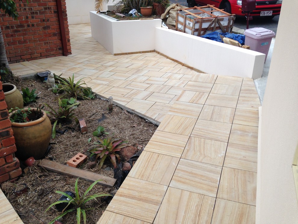 Large contemporary front patio in Brisbane with natural stone paving and no cover.