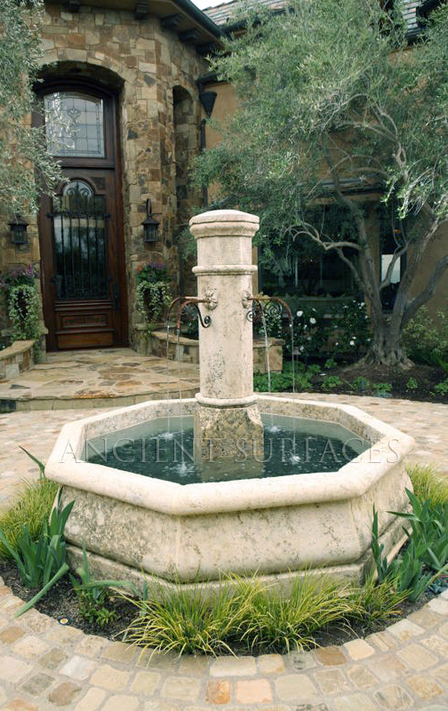 Medelhavsstil inredning av en mellanstor uteplats framför huset, med en fontän och naturstensplattor
