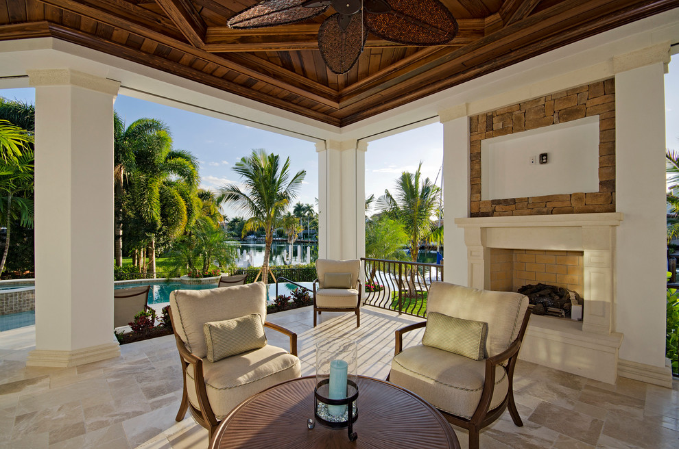 Esempio di un patio o portico tropicale dietro casa con pavimentazioni in pietra naturale, un tetto a sbalzo e un caminetto
