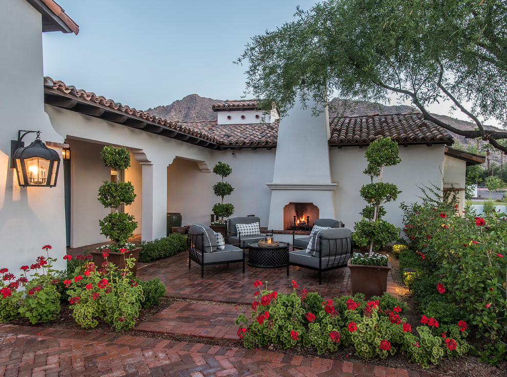 This is an example of an expansive mediterranean courtyard patio in Phoenix with brick paving, no cover and a fireplace.