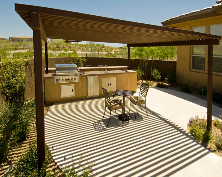 This is an example of a medium sized back patio in Phoenix with an outdoor kitchen, concrete paving and a pergola.
