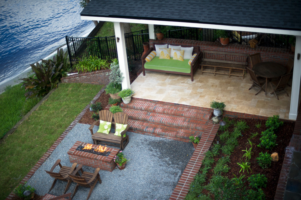Réalisation d'une grande terrasse arrière minimaliste avec un foyer extérieur, un gravier de granite et une extension de toiture.