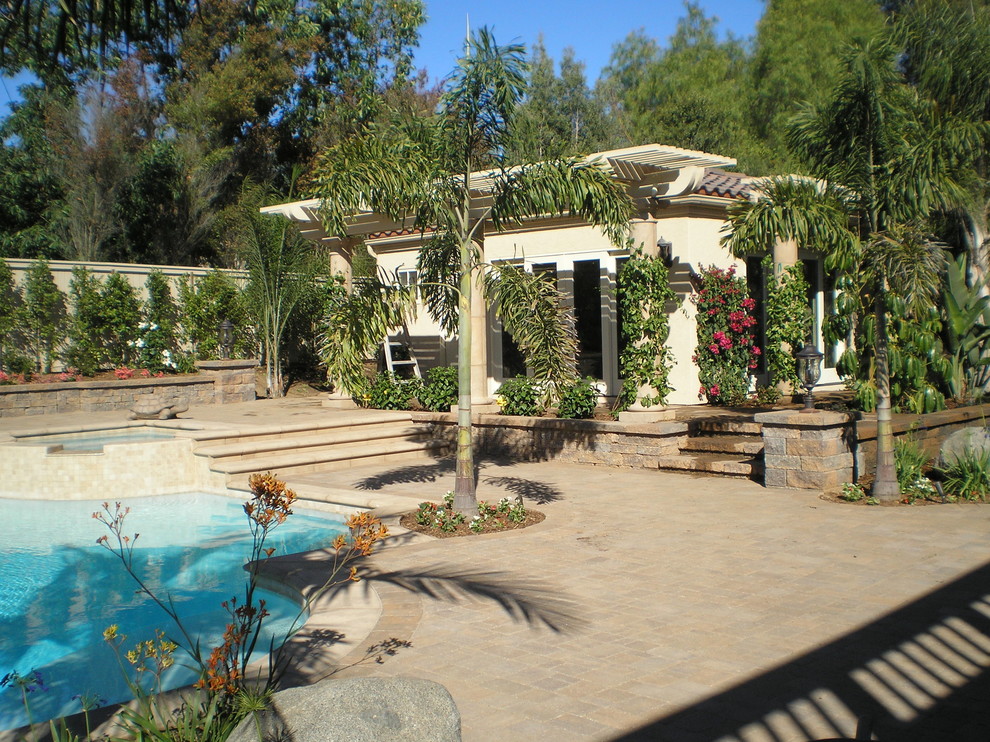 Idee per un grande patio o portico tropicale dietro casa con fontane, cemento stampato e un parasole