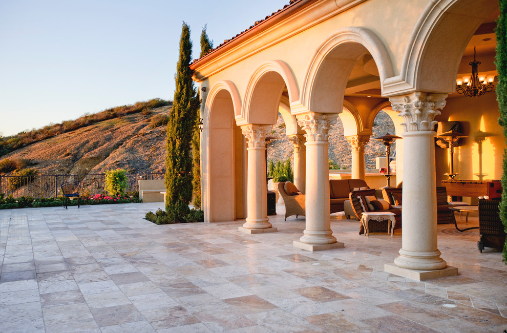 Photo of an expansive mediterranean back patio in Orange County with a fire feature, natural stone paving and a roof extension.