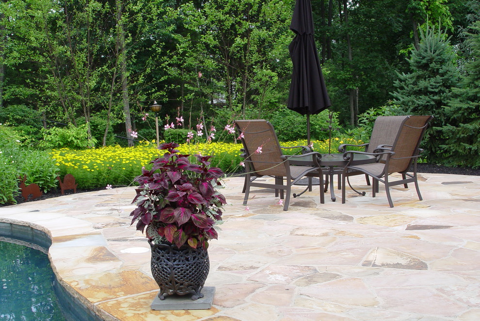 Example of a mid-sized island style backyard stone patio fountain design in New York with no cover