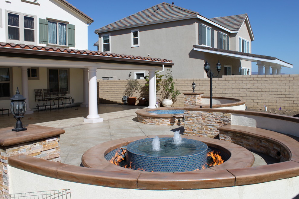 Immagine di un ampio patio o portico design dietro casa con fontane, cemento stampato e un parasole