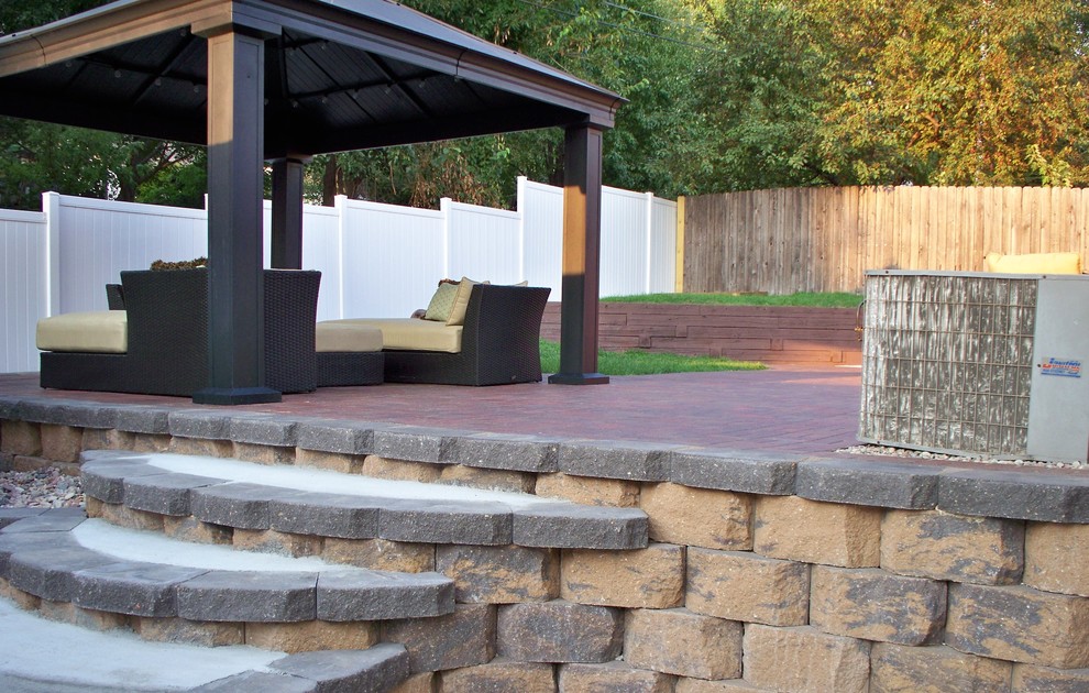 Foto di un ampio patio o portico minimalista dietro casa con un focolare, pavimentazioni in mattoni e un gazebo o capanno