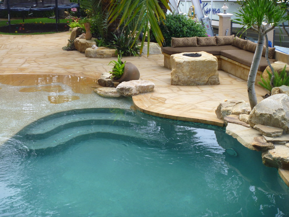 Inspiration for a contemporary back patio in Miami with natural stone paving and a roof extension.