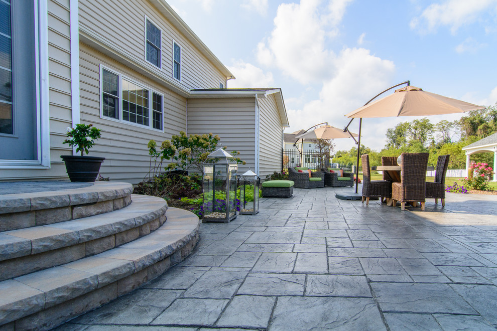 Idee per un ampio patio o portico classico dietro casa con cemento stampato e una pergola