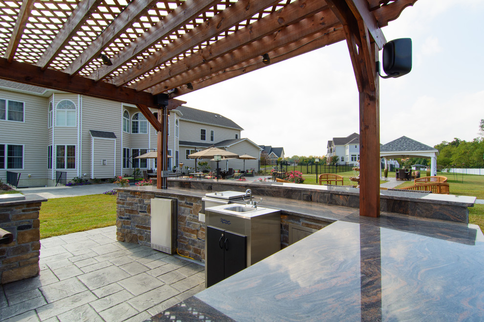 Foto di un ampio patio o portico tradizionale dietro casa con cemento stampato e una pergola