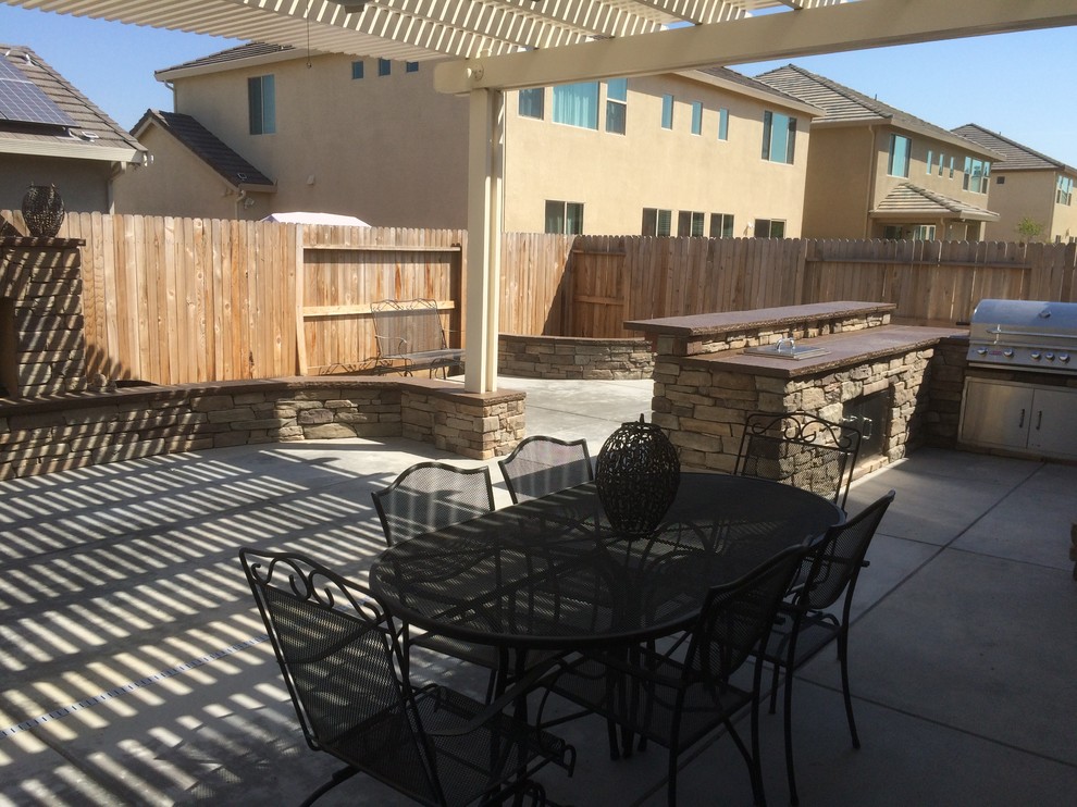 Large classic back patio in Other with an outdoor kitchen, concrete slabs and a pergola.