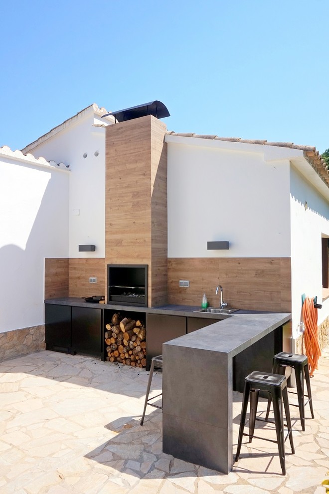 Réalisation d'une grande terrasse latérale méditerranéenne avec une cuisine d'été, des pavés en pierre naturelle et aucune couverture.