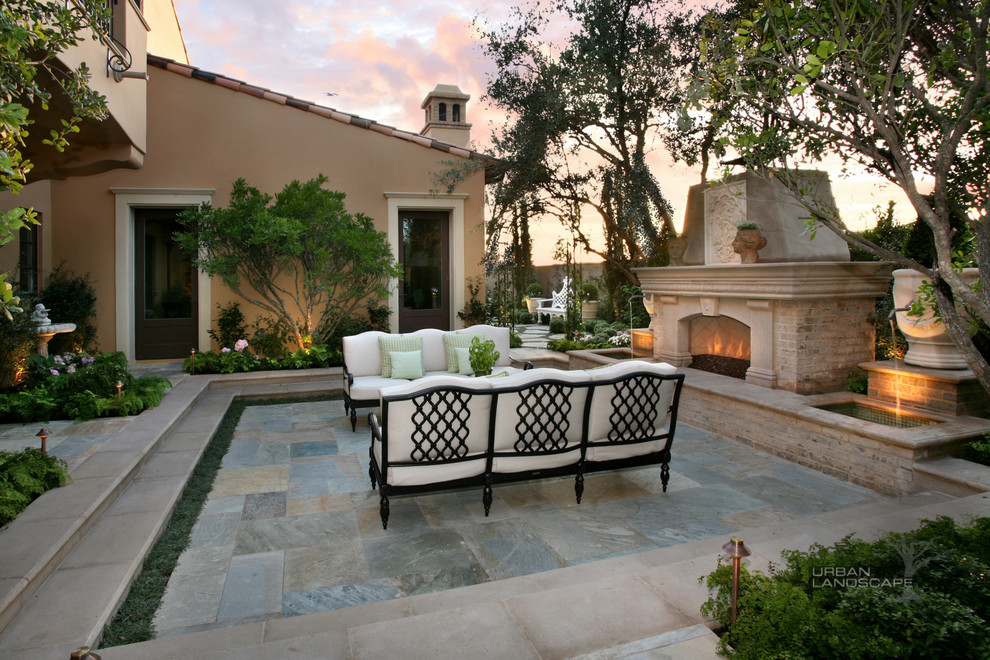 This is an example of a large classic courtyard patio in Orange County with a fire feature, natural stone paving and no cover.