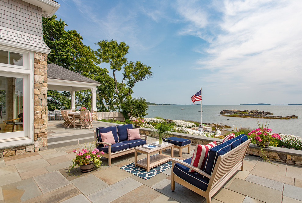 Example of a huge beach style backyard stone patio design in Boston with a roof extension