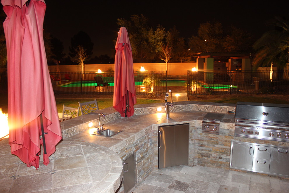 This is an example of a large back patio in Phoenix with an outdoor kitchen, brick paving and no cover.