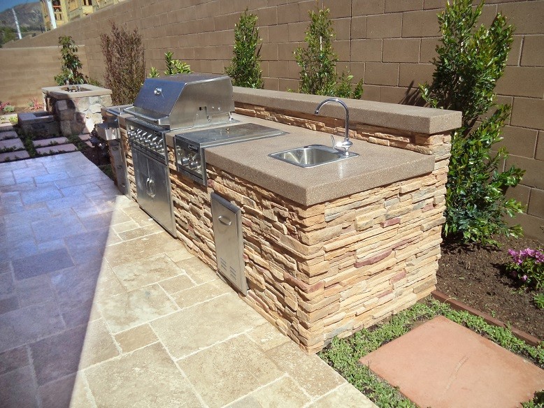 Inspiration for a contemporary backyard stone patio kitchen remodel in Orange County