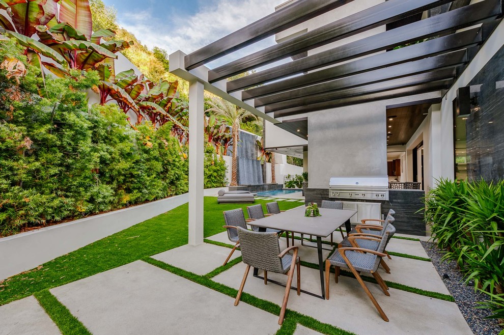 This is an example of an expansive contemporary back patio in Los Angeles with an outdoor kitchen, concrete paving and a pergola.