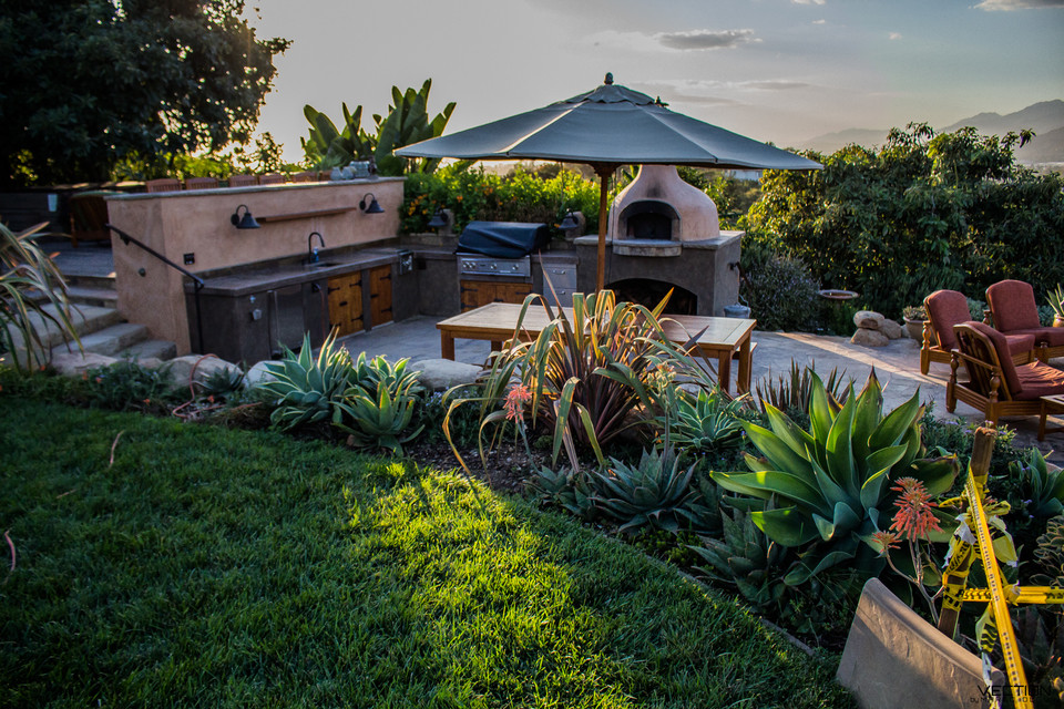 Cette photo montre une grande terrasse arrière sud-ouest américain avec une cuisine d'été, des pavés en pierre naturelle et aucune couverture.