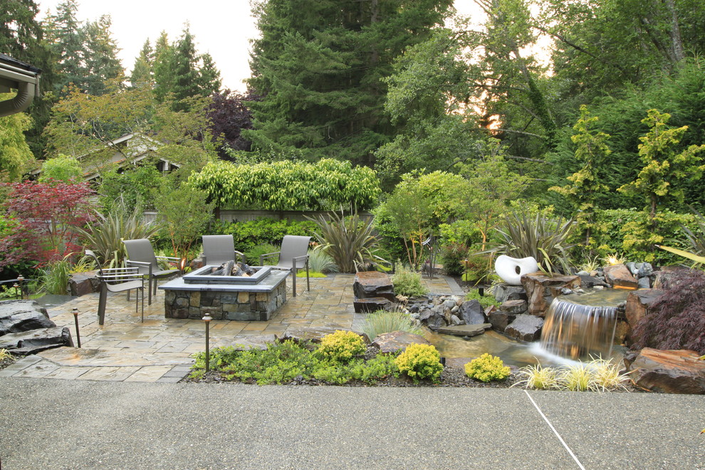 Imagen de patio tropical de tamaño medio sin cubierta en patio trasero con fuente y adoquines de piedra natural