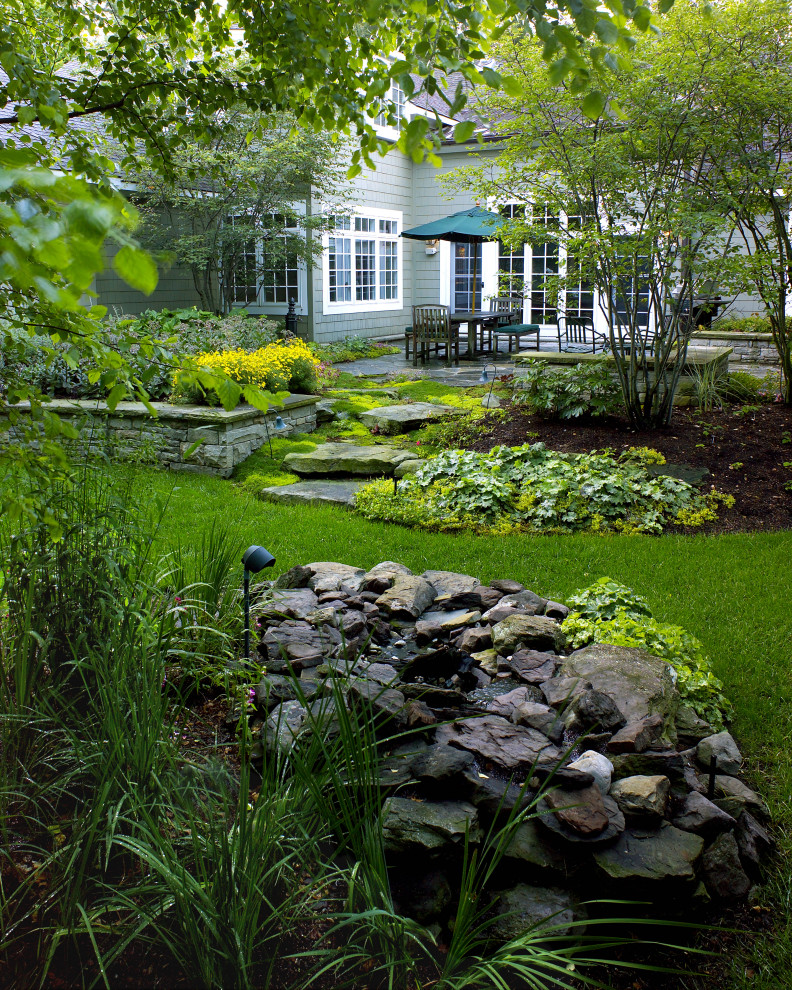 Diseño de jardín rural en patio trasero con fuente y adoquines de piedra natural