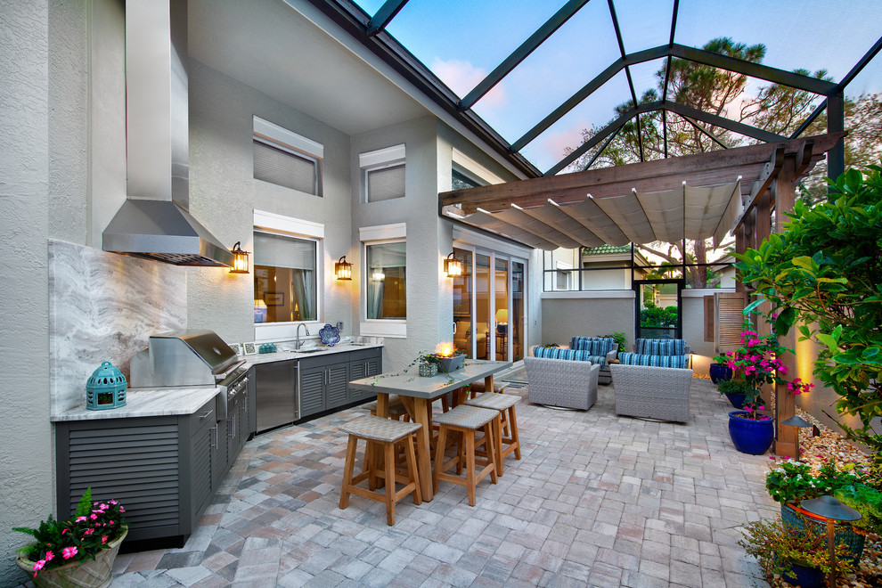 Example of a large transitional backyard concrete paver patio kitchen design in Miami with a pergola