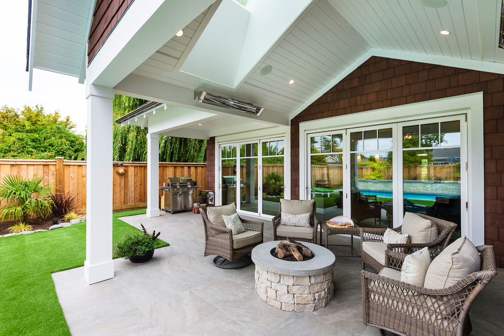 Immagine di un patio o portico stile marino di medie dimensioni e dietro casa con un focolare, piastrelle e un tetto a sbalzo