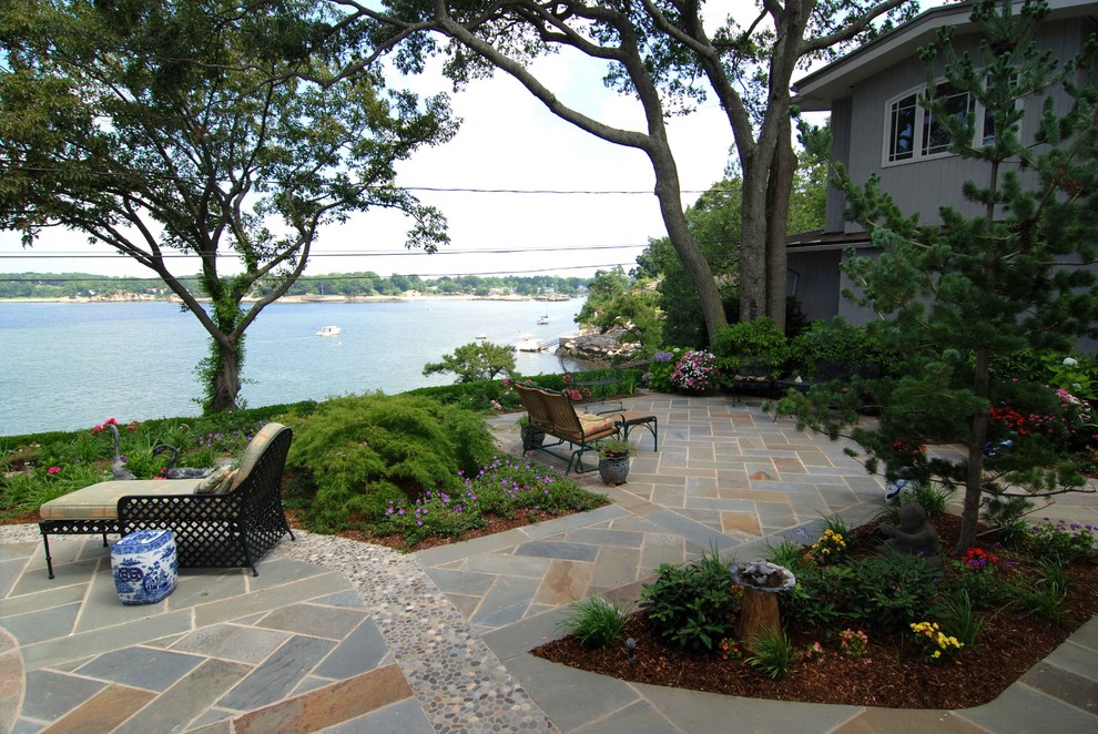 Ejemplo de patio costero grande sin cubierta en patio trasero con adoquines de piedra natural