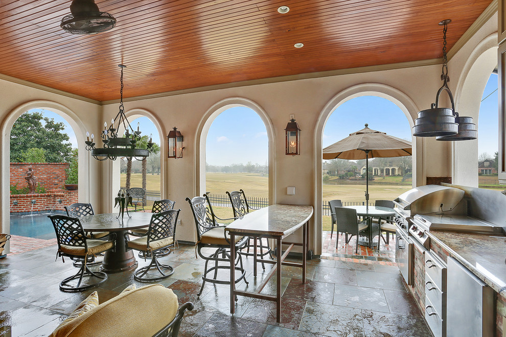 Cette image montre une grande terrasse arrière traditionnelle avec une cuisine d'été, des pavés en pierre naturelle et une extension de toiture.